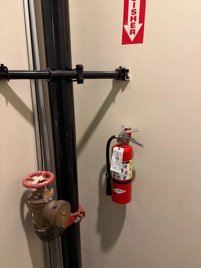 Wall-mounted fire extinguisher next to standpipe valve at a Mission District apartment building in San Francisco, CA.
